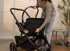 Person pushing a black stroller indoors with a neutral background