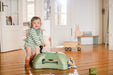 Child standing next to green ride on toy in living room setting