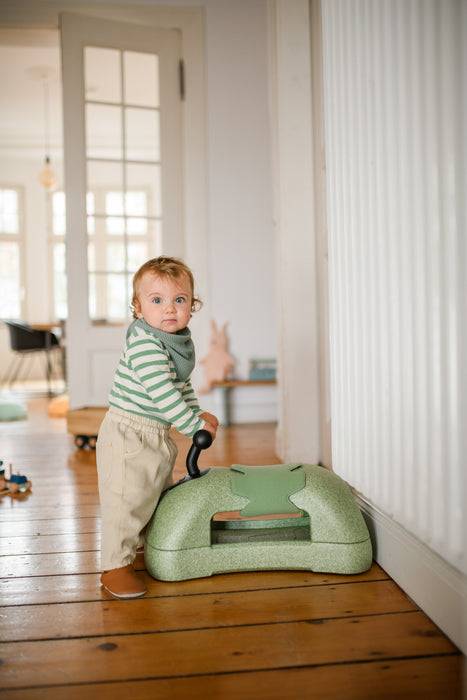 Child standing in front of green ride on toy in living room setting