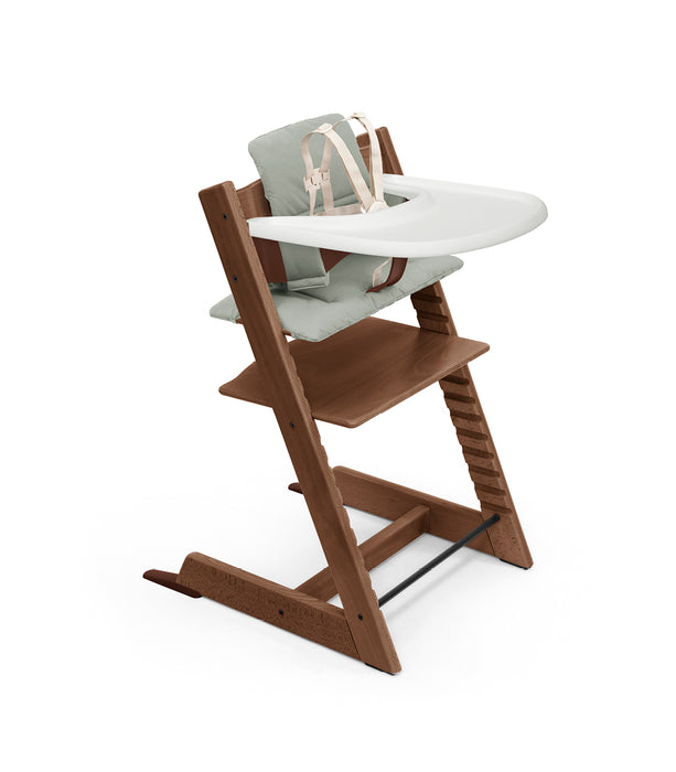 Dark brown wooden high chair with a white tray and green cushion on a white background