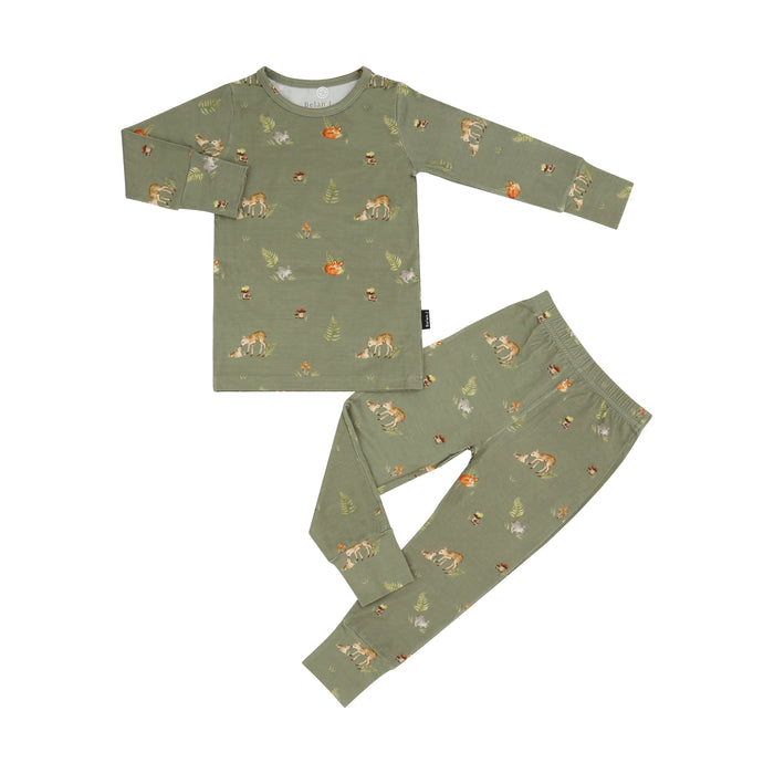 A two-piece children's pajama set in sage green, featuring a long-sleeve top and matching pants with an all-over woodland print of foxes, rabbits, and mushrooms, laid out on a solid white background.