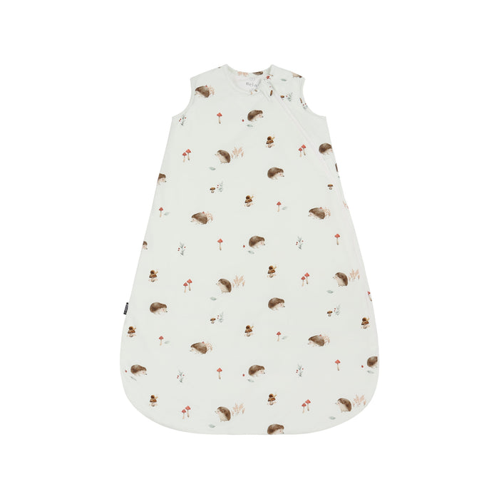 A sleeveless baby sleep sack with an all-over woodland print of hedgehogs, mushrooms, and small trees on an off-white background, shown flat against a white studio background.