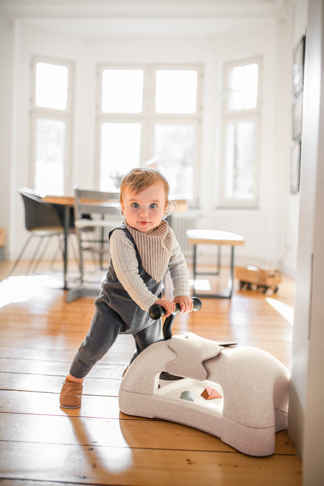 Child scooting cream coloured ride on toy across wooden floor
