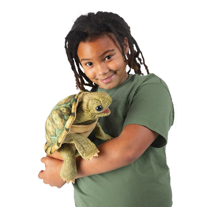 Child holding a turtle puppet against a white background