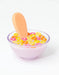 Clear glass bowl with colorful cereal loops and a wooden spoon on a white background