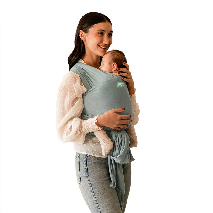 Woman holding a baby in a grey moby baby carrier against a white background