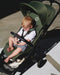 Child sitting in a green stroller on a sidewalk