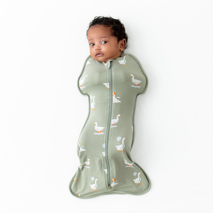 Baby in a green swaddle with duck pattern on a white background