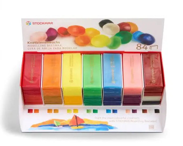 A display box of STOCKMAR modeling beeswax (natural modeling clay) containing individually wrapped pieces of beeswax.  The display features six vertical columns of colorful wax sticks in red, orange, yellow, green, blue, and pink, with a white header card showing the brand logo and product details.