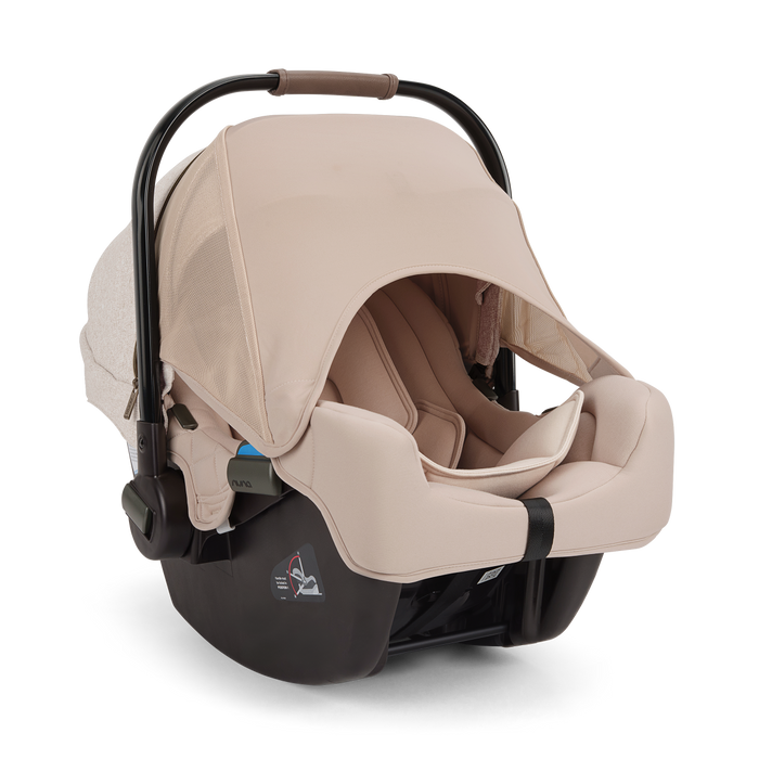 A Nuna baby car seat in a light beige fabric with a black base, shown on a clean white background.
