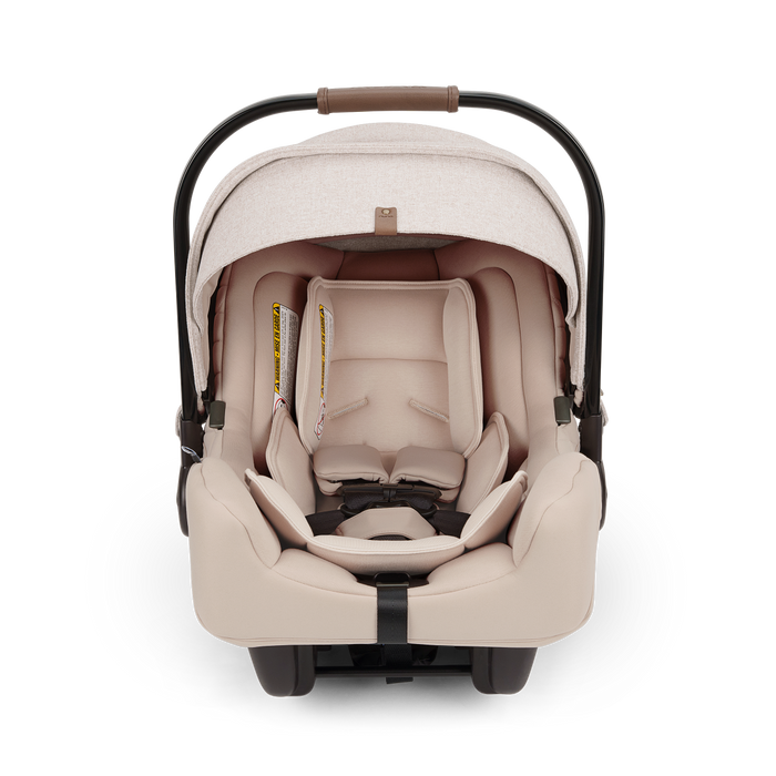 A Nuna baby car seat in a light beige fabric with a black base, shown on a clean white background.