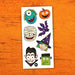 A sheet of Halloween-themed stickers featuring cartoon monsters, a pumpkin, a mummy, a bat, a witch, a vampire, and Frankenstein's monster, displayed on an orange wood background.