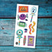 A sheet of colorful Halloween-themed temporary tattoos or stickers displayed flat on a rustic, weathered blue wooden surface. The sheet features cartoon illustrations of a jack-o'-lantern, ghost lollipop, purple skull candy, green Frankenstein monster, orange and yellow striped snake, and a skull-and-crossbones on a purple flag.