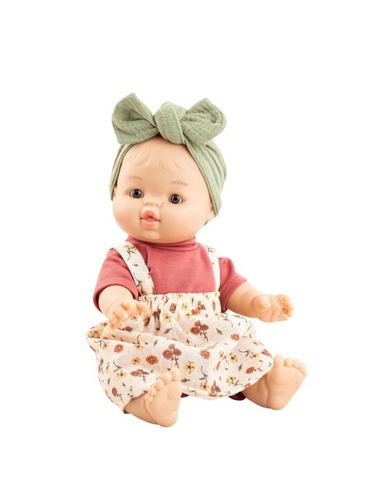 Baby doll wearing a pink shirt and floral overalls with a green headband on a white background