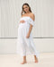 Woman wearing a white off-shoulder maternity dress against a minimalistic background