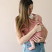 Woman holding a baby in a pink sling against a plain background