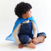 Child wearing a blue silk as a cape sitting on a white floor