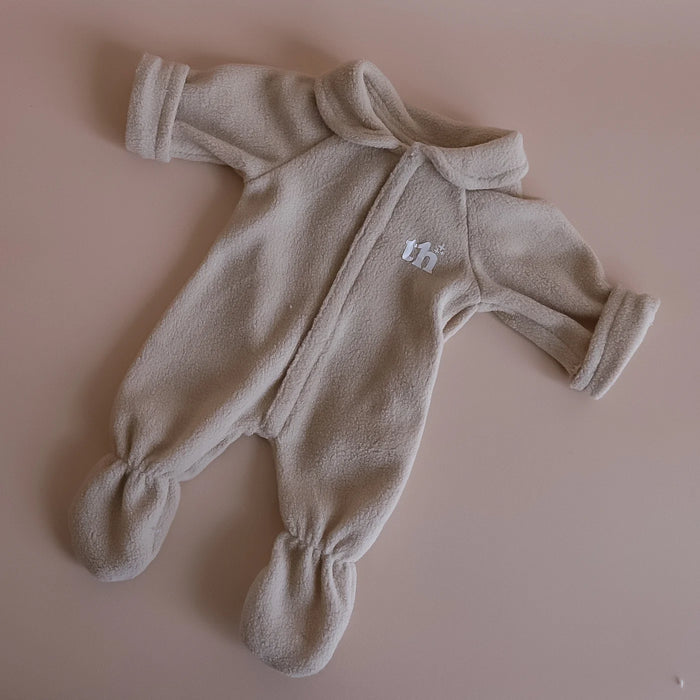 Beige baby doll onesie with a small logo on a pink background