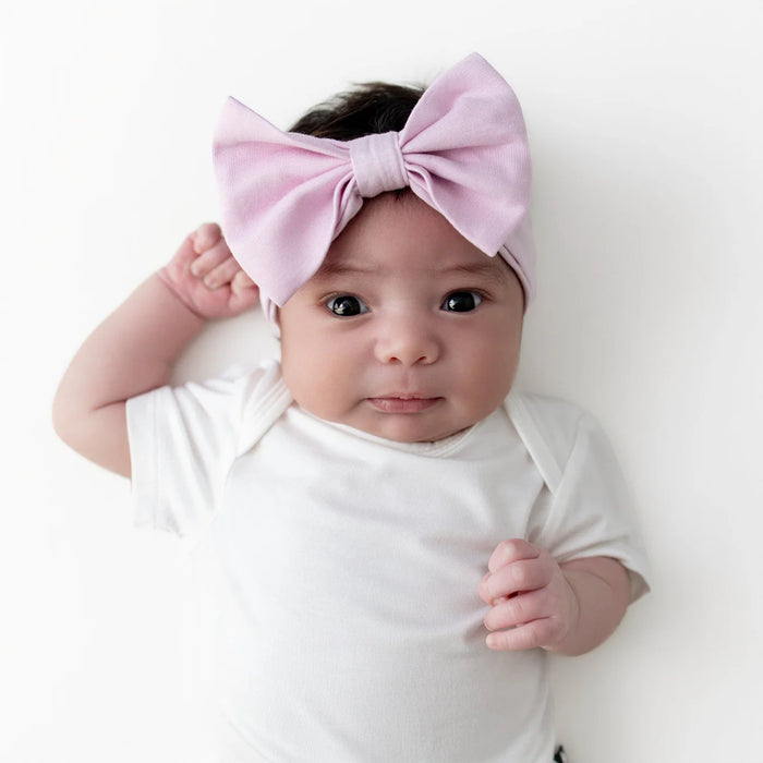Baby wearing a white onesie and a large pink bow headband on a white background
