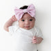 Baby wearing a white onesie and a large pink bow headband on a white background
