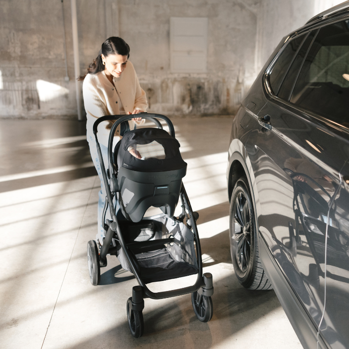Woman walking a stroller nearer to a car in a sunlit indoor partking garage