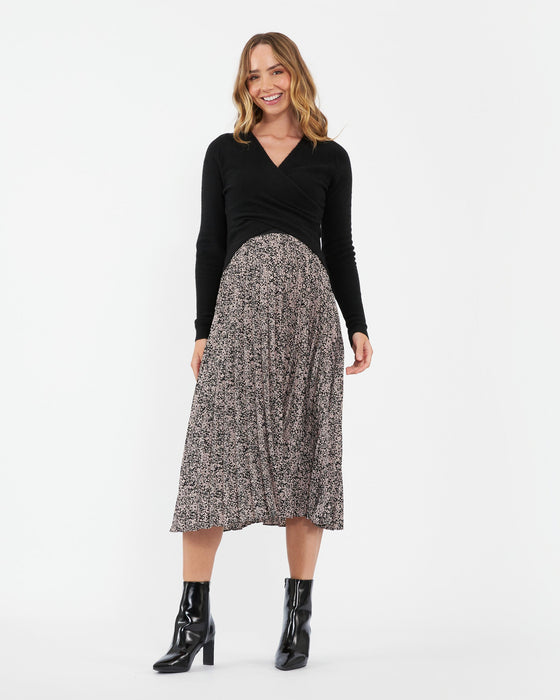 Woman with long black sweater standing with small print floral pleated skirt.