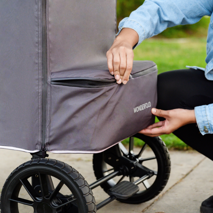 Person zippering a gray weather cover on a stroller wagon with 'WonderFold' branding.