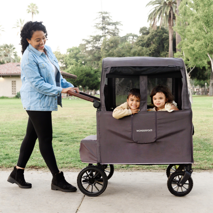 Woman pushing a wagon stroller with two children in a park