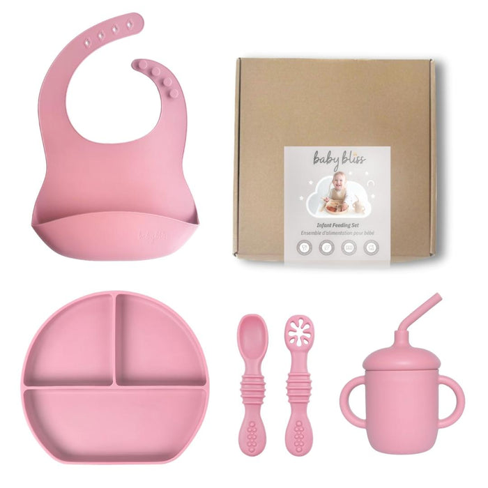 Pink baby feeding set with bib, plate, spoons, and cup on a white background