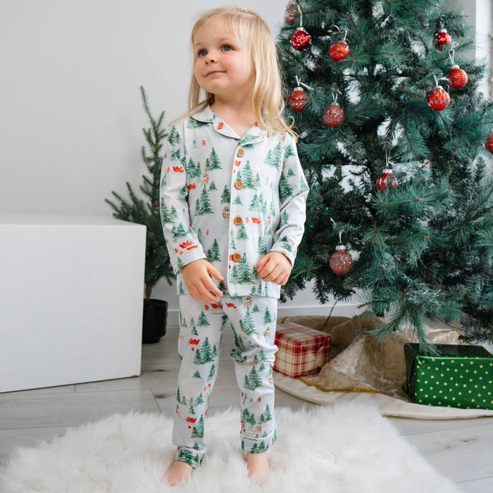 Child wearing Christmas-themed pajamas standing in front of a decorated Christmas tree.