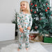 Child wearing Christmas-themed pajamas standing in front of a decorated Christmas tree.