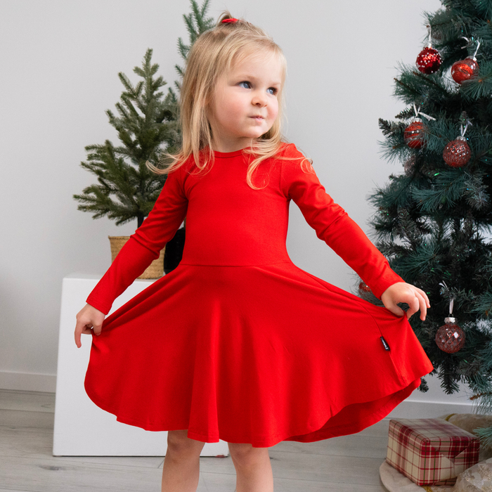 Young girl in a red twirl dress standing in front of decorated Christmas trees.