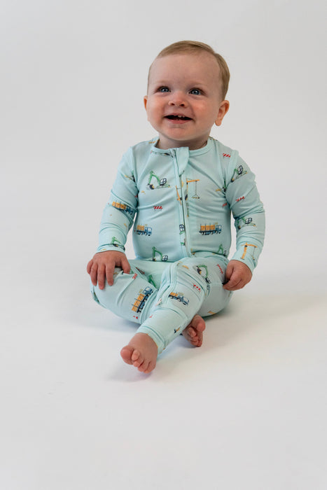 Baby wearing a light blue pajama set with vehicle prints on a white background