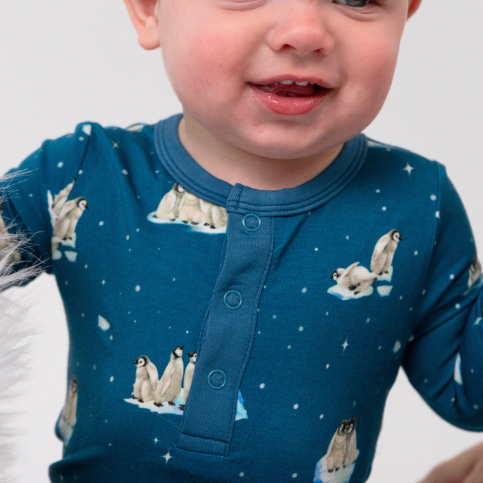 Child wearing a blue pajama with penguin design on a plain background
