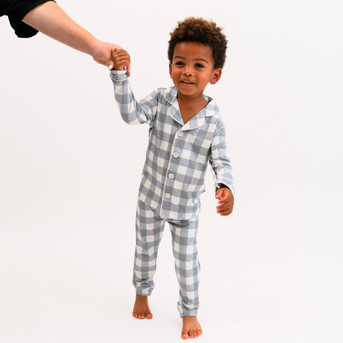 Child wearing blue and white checkered pajamas holding hands with an adult on a white background