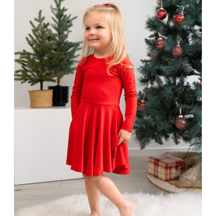 Young girl in a red dress standing in front of a decorated Christmas tree.