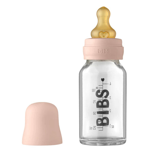 A clear glass baby bottle with a measurement scale, nipples, and a cap, branded with the name 'BIBS'.