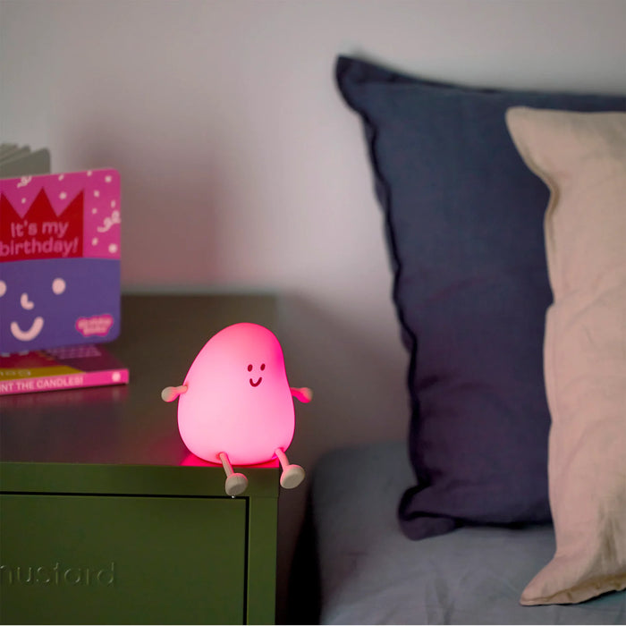 Pink night light on a bedside table with pillows and a book in the background