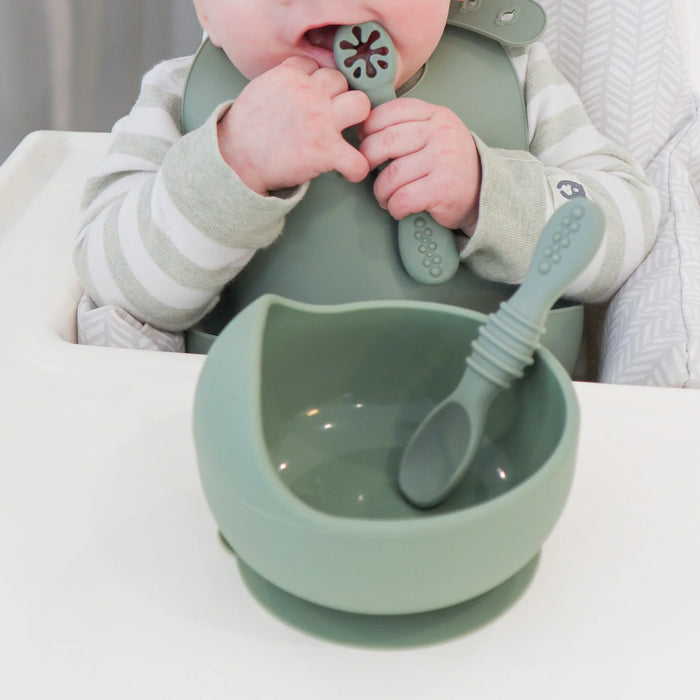 Child grasping infant feeding spoon with bowl and spoon nearby on highchair tray
