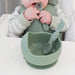 Child grasping infant feeding spoon with bowl and spoon nearby on highchair tray
