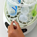 Hand placing a detergent tablet into a white bottle sterilizer with bottles inside.