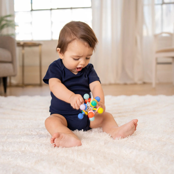 Baby playing with a colorful toy on a white carpet in a bright room.