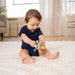 Baby playing with a colorful toy on a white carpet in a bright room.