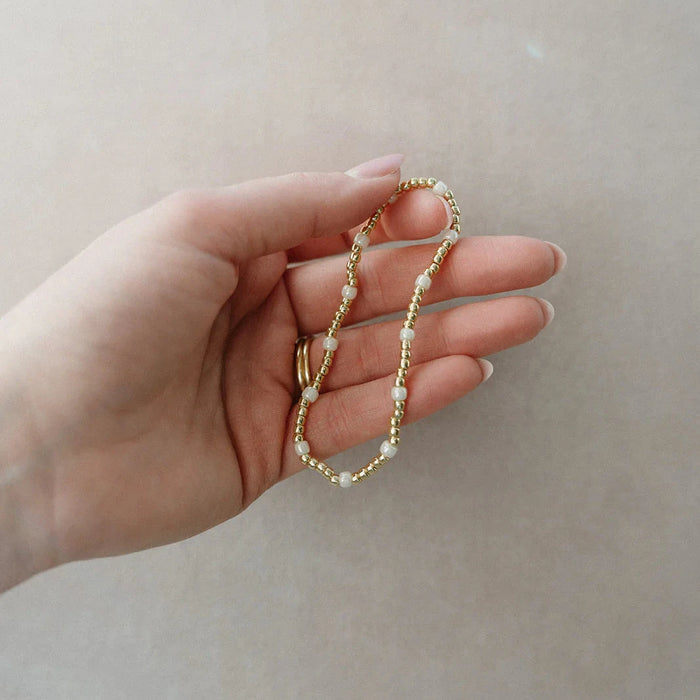 Hand holding beaded bracelet with ivory and gold beads against a light background
