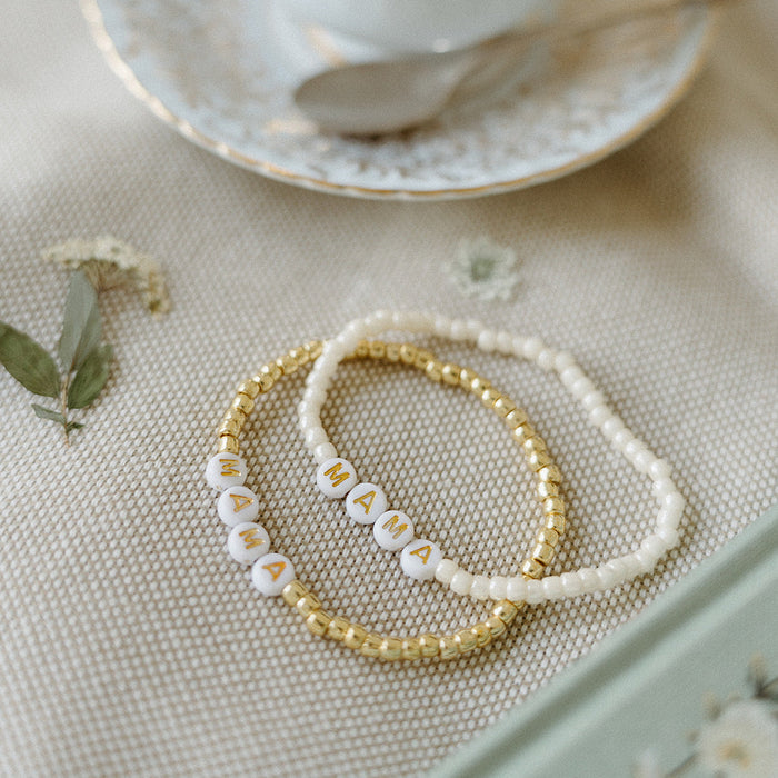 Two beaded bracelets set against a brunch table with a small flower and tea saucer. 