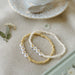 Two beaded bracelets set against a brunch table with a small flower and tea saucer. 
