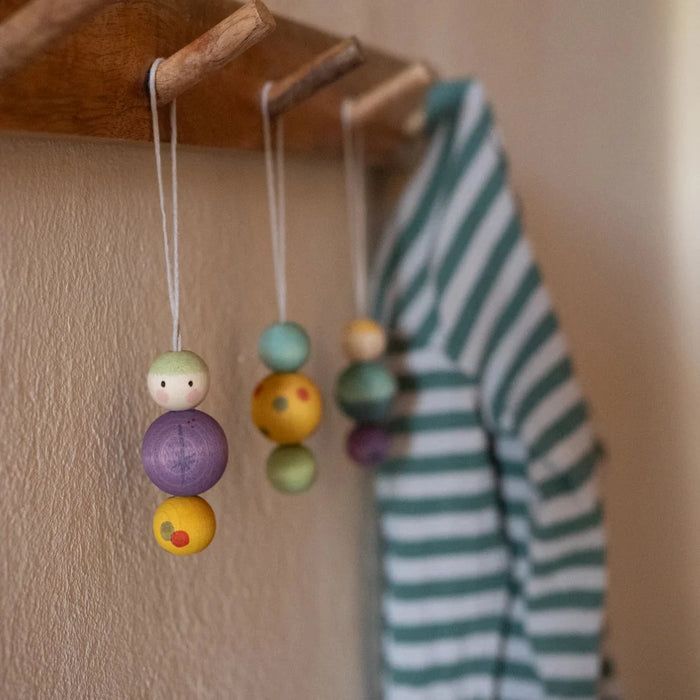 A clothes hook on a wall shows decoration of holiday ornaments with Snow man shaped wooden ball connected by string