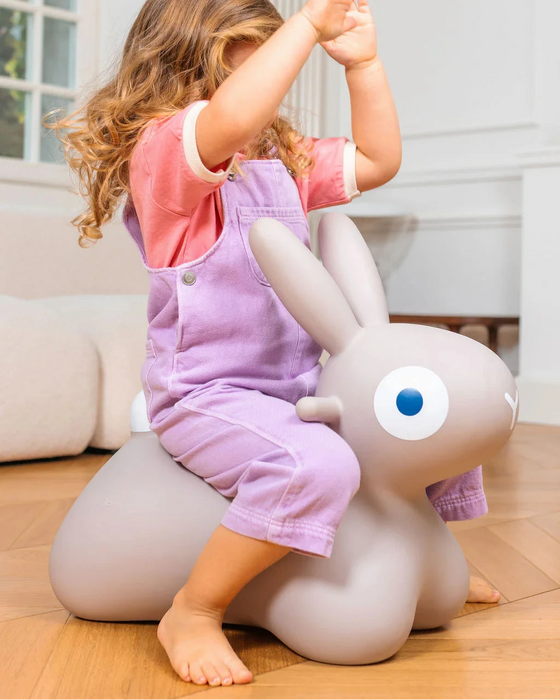 Child sitting on a gray inflatable bunny toy indoors.