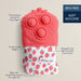 Red silicone baby product with strawberry patterned pouch on beige background