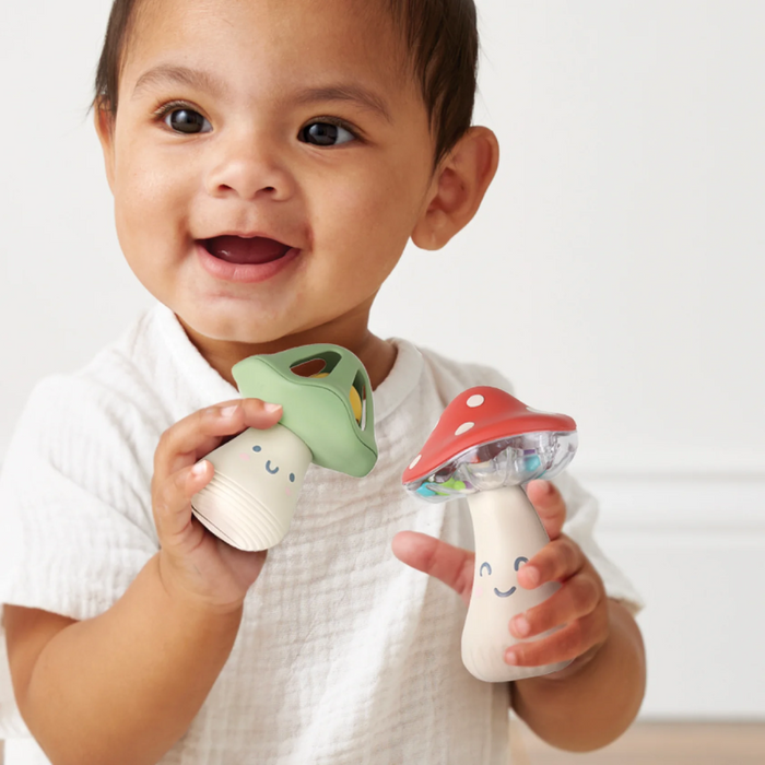 Child holding two colourful mushroom shaker toys against a plain background